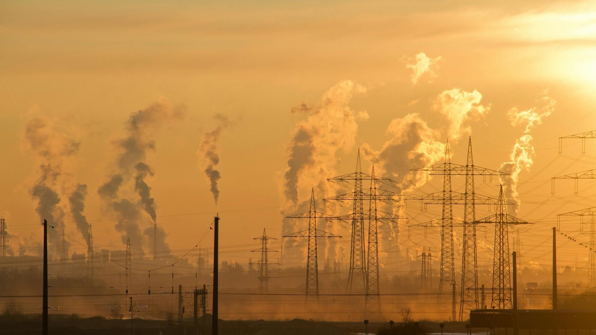 power lines with plumes of factory smoke at sunset