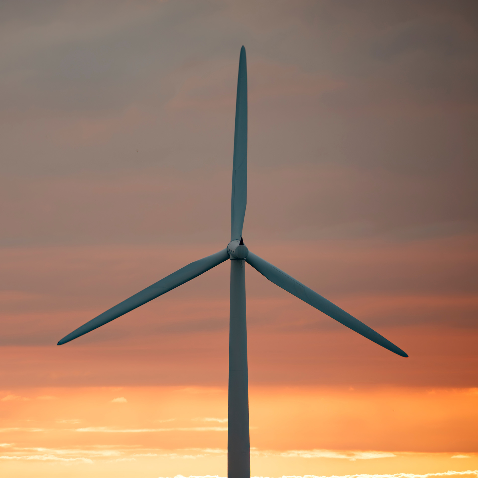 A solitary wind turbine against an overcast sky and fiery orange sunset