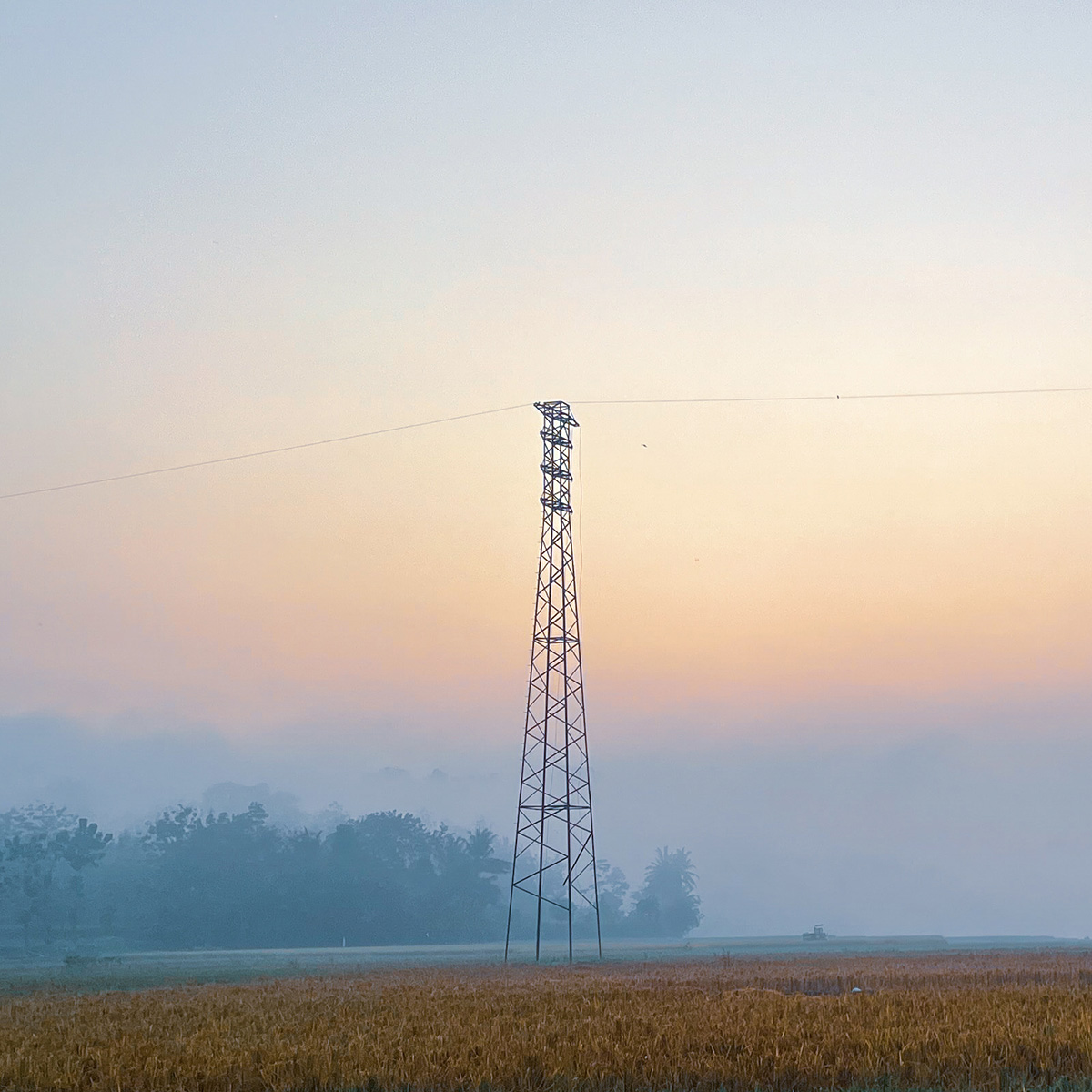 A lone transmission tower stands over a misty farm field at dawn