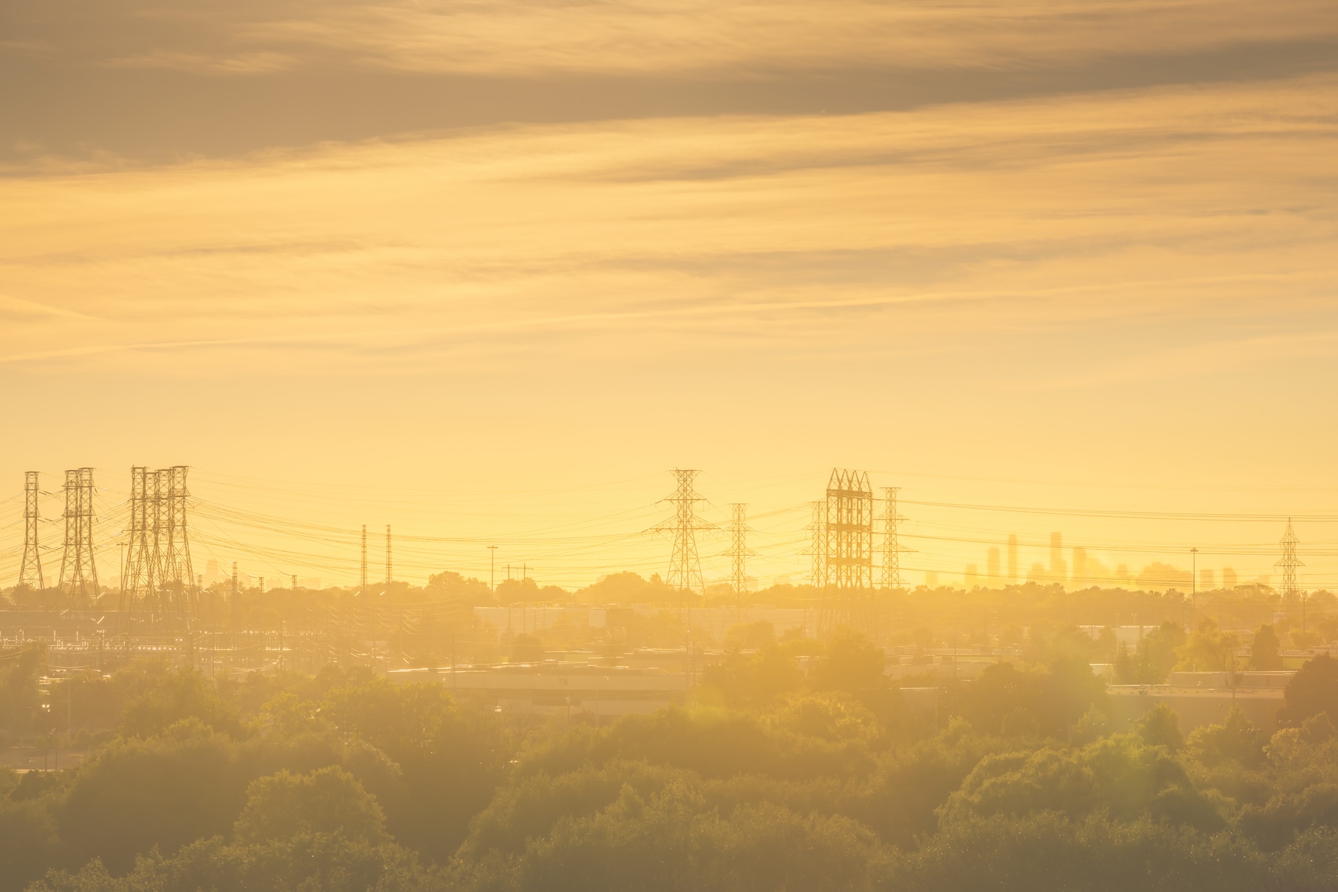 Power lines and a distant city skyline in silhouette against a hot, hazy, yellow-orange sunset